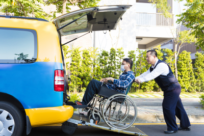 driver helping man on wheelchair getting into car