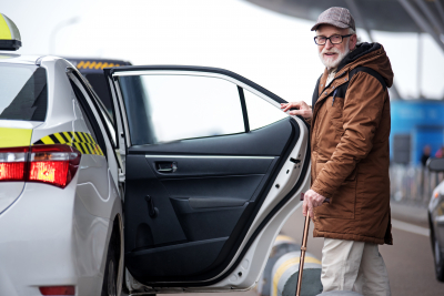 portrait of positive bearded old man in glasses going to sit into the car